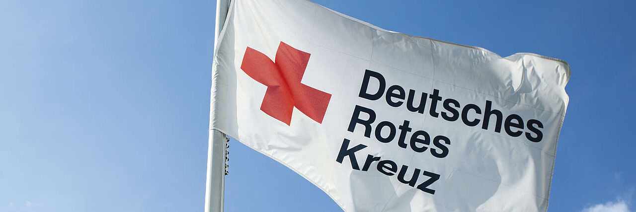 Bühnenbild Rotkreuzflagge Rot-Kreuz-Fahne mit Logo weht vor blauem Himmel im Wind